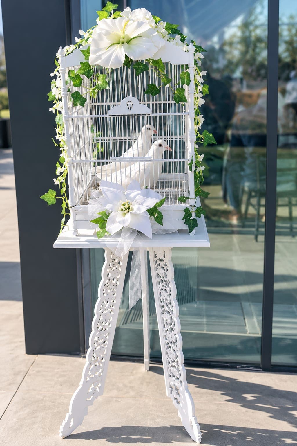 An ornate white birdcage holding two doves, trimmed with ivy and white lilies