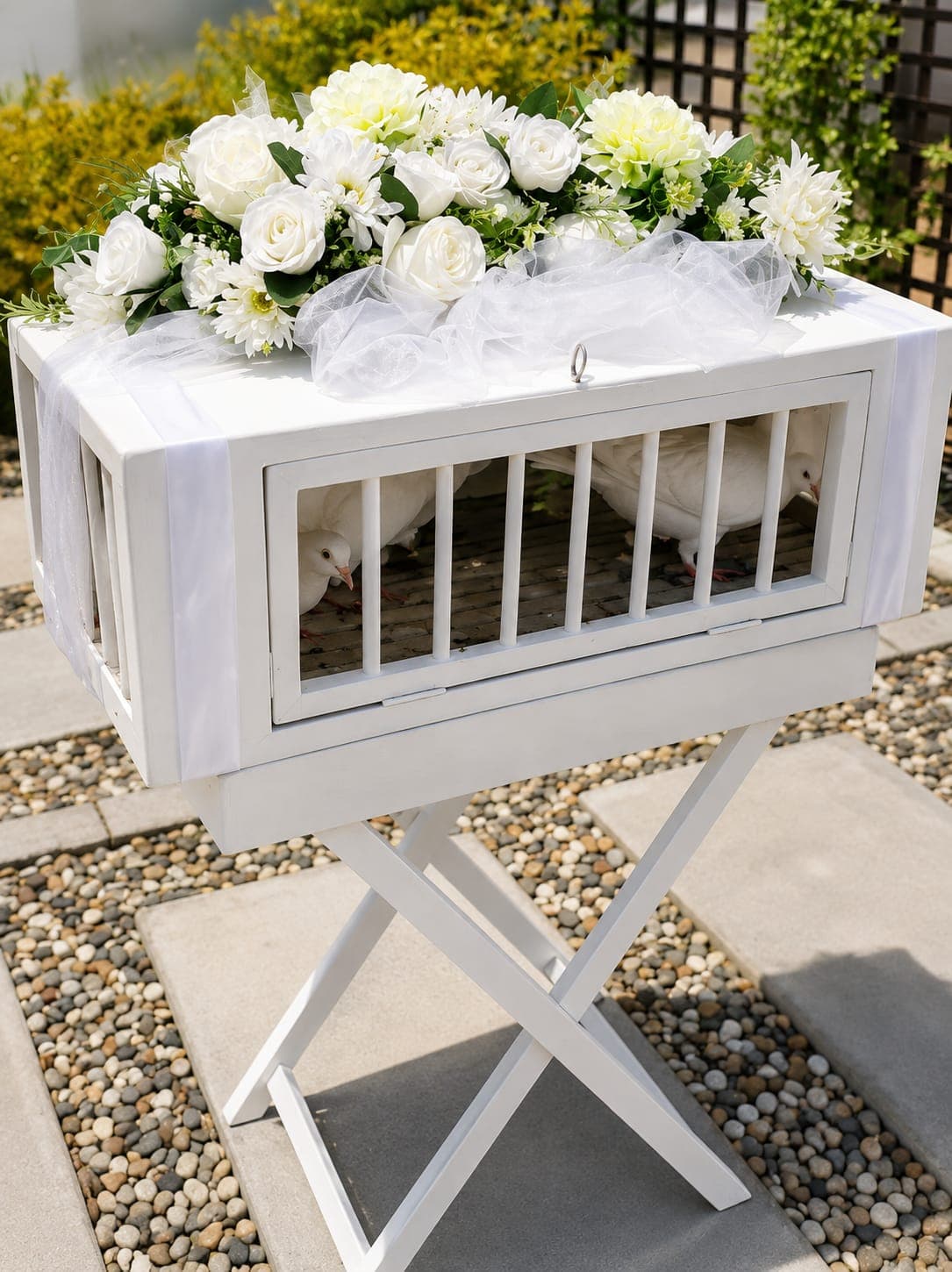 A white release cage of doves decorated with roses and organza, set in a garden